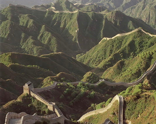 A breathtaking view of the Great Wall of China winding through lush green hills under a warm sunlight.