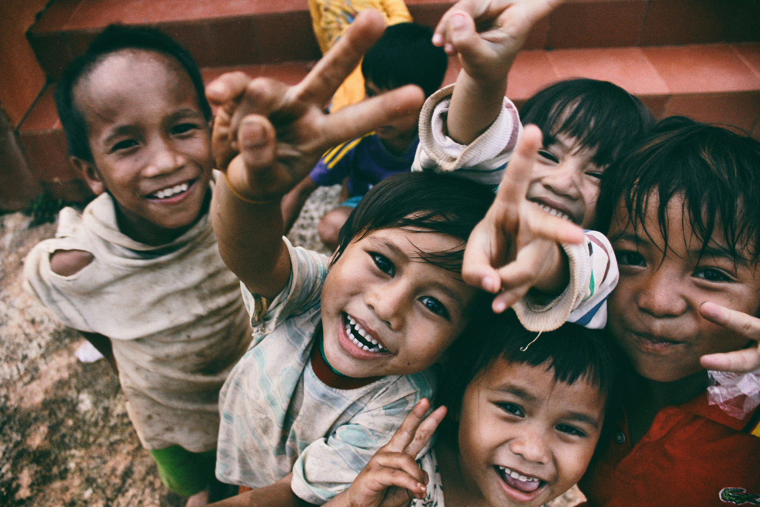 Group of smiling children making peace signs, representing our commitment to donating 10% of profits to charity.